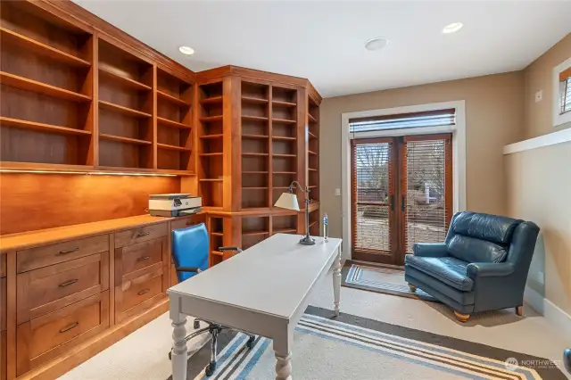 Large den/office with ample built-in shelving and cabinets, looking out onto the landscaped yard.