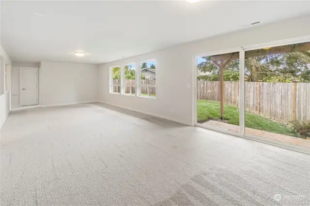Family room with carpet throughout. Glass slider leads to outdoor patio and backyard.