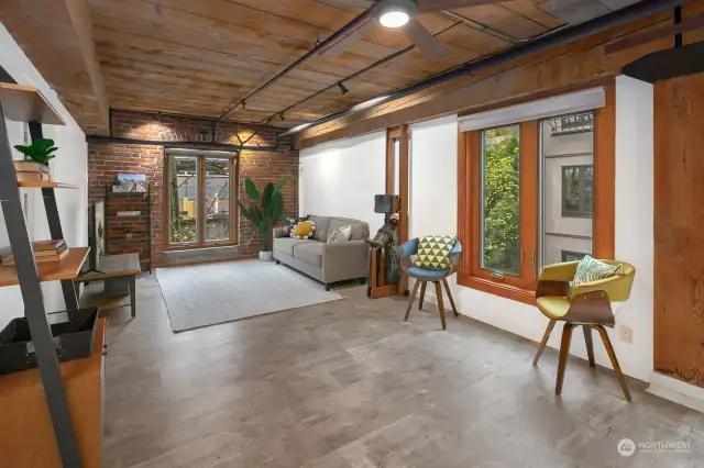 Loft style living area with exposed brick, wood ceilings and old-growth beams opens to eat-in kitchen and extra-large private patio.
