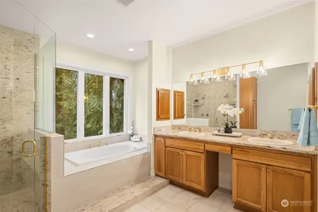 Primary 6-piece bathroom with big windows and lots of natural light. A 5-foot bathtub, dual sinks, stone tile, and granite accents. A shower featuring dual shower heads  and granite walls. Connected to a water closet with a new light and exhaust fan (2024).
