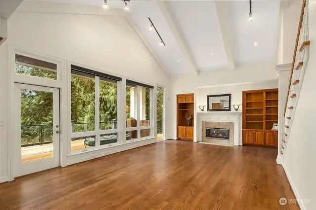 Great Room has high vaulted ceilings, a wall of windows, and a door leads to the rear deck. Gas fireplace with a granite surround, and custom mill work. Wood cabinetry for display and storage.