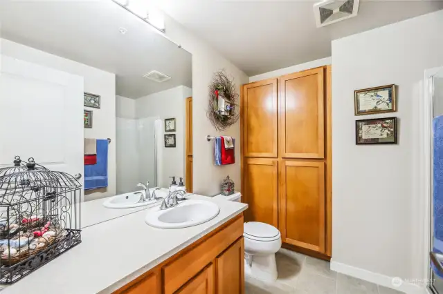 The guest bath features a large vanity, shower with glass enclosure, gorgeous wood cabinets, and tiled floors.