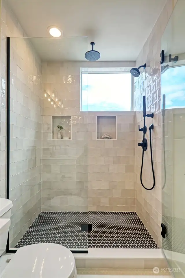Recently retiled to add a second niche and incorporate custom tiles, this walk-in shower features a rain shower,  double spray wall mounted fixtures and a large window.