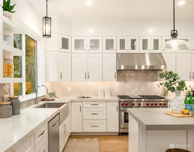 Beautiful white shaker cabinets, under  cabinet lighting, glass doors at the top and  open shelving for display compliments this  luxurious yet comfortable kitchen outfitted  with top of the line stainless appliances.