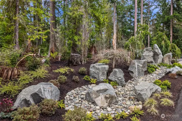 Front yard landscape features native  plantings and assorted landscaping boulders  and logs.