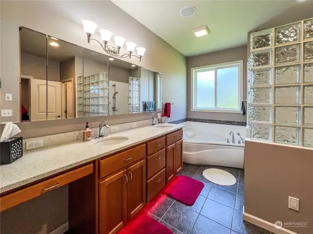 Primary Suite bath featuring hard surface counters, double sinks, makeup area, radiant heat floors, jetted tub and large walk in shower.
