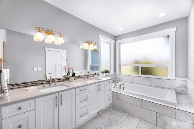 Light and airy primary bath with double vanity, jet tub, large frosted windows.