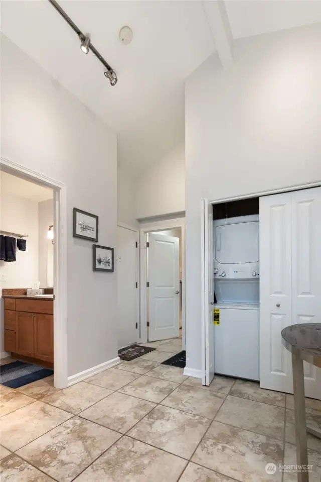 Another view of the entrance to the home showing the washer and dryer, hallway full bath to the left of the photo and doorway to the primary suite & bath featured in the back of the photo.