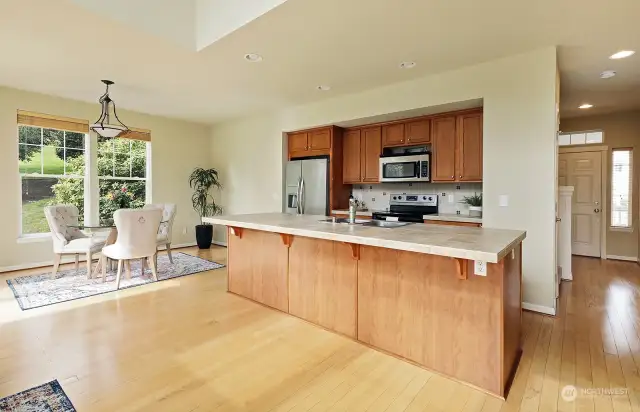 Countertops are ceramic tile, cabinets are maple, newer stainless appliances. Center island has enough space for additional dining space.  Front door is viewed in the distant right of this photo.