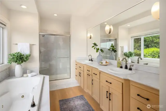 Bright and luxurious primary bath with solid countertops, double vanity, jetted tub, walk-in shower, and private water closet