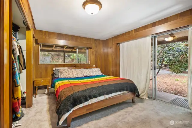 The bedroom features a whole wall of closet space, wood paneling, and a large slider leading outdoors.