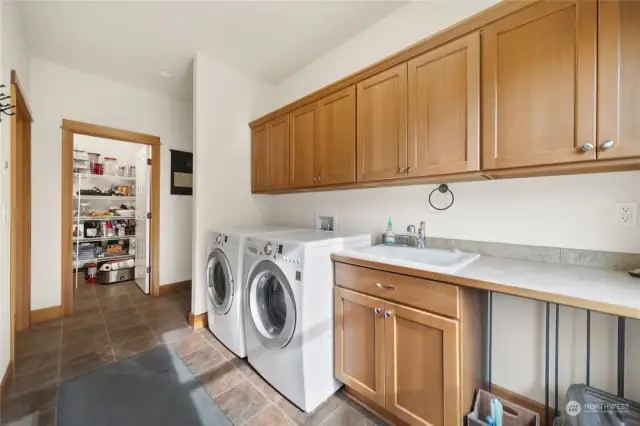 Huge laundry room with lots of cabinets, utility sink, and the full pantry is in the foreground.