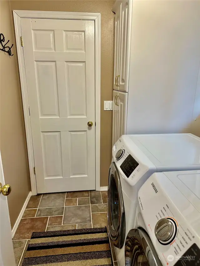 Laundry area with tile floor, storage cabinet and washer & dryer.  The door in this photo opens to the large garage.
