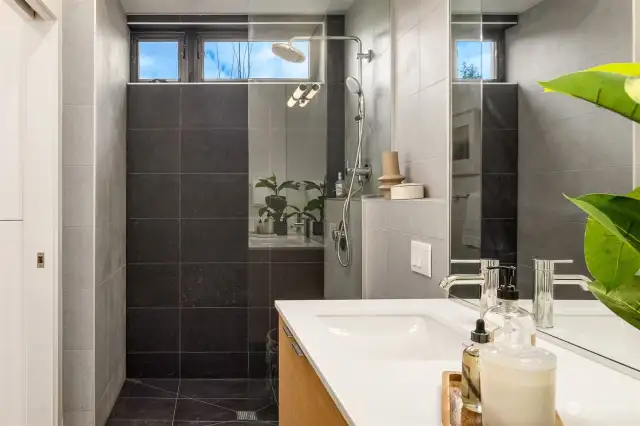 The bathroom maintains a consistent level of luxury including Abodian cabinetry, quartz countertops, ceramic tile floors, and Grohe WaterSense fixtures, reflecting a commitment to quality and sophistication that runs throughout the home.