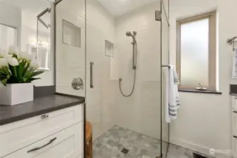 Frameless glass, walk-in shower is beautifully tiled. Additional counter and cabinetry complements the room.