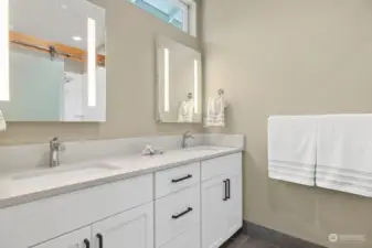 LED mirrors highlight dual sink vanity & heated tile floor with glass barn door for shower & toilet compartments