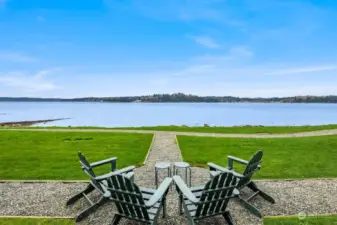 Relax and enjoy the scenic view of Rich Passage from the comfort of Adirondack chairs, creating a perfect spot to unwind and take in the natural beauty of the surroundings.