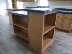 A View of the Very Spacious Chef Storage Prep Island Kitchen with Oak Wood Cabinets, Tile Cabinet Edging, New Paint, Trim, and Vinyl Plank Flooring.