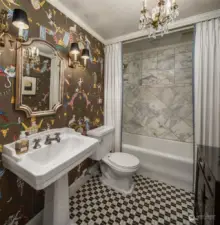 A newly remodeled full bath features designer tile and wallpaper as well as a gorgeous petite chandelier.