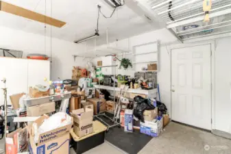 Two car garage with work bench and storage. Door leads to covered back patio and backyard.