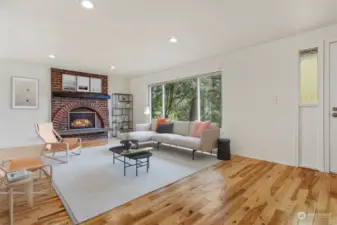 Formal living room with a gas fireplace, hardwood floors and recessed lights.  Opens to dining room.  Virtually staged photo.