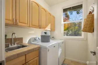 The laundry room is right off of the garage, acting as a mud room. Well appointed with a tile counter, stainless steel sink and wood cabinets.