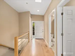 View towards front door from stair landing, coat closet visible just inside on left, door to guest bathroom on right, door nearest on right side leads to massive primary suite.