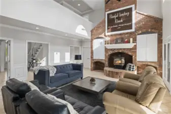 Soaring vaulted ceilings and a gorgeous brick wall/fireplace backdrop grace the great room. A TV is cleverly stowed behind the double cabinet door to the right of the fireplace.