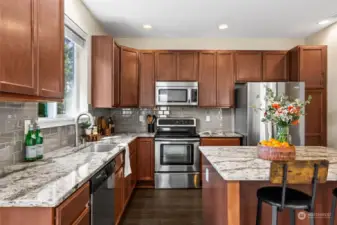 Gorgeous granite slabs harmonize seamlessly with the glass tile backsplash and 42-inch kitchen cabinetry, creating an elegantly finished appearance.