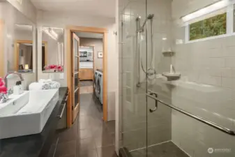 Primary ¾ bath with heated ceramic tile floor, Toto bidet and glass shower. Laundry room washer/dryer can be seen in next room. Beyond that is the kitchen.