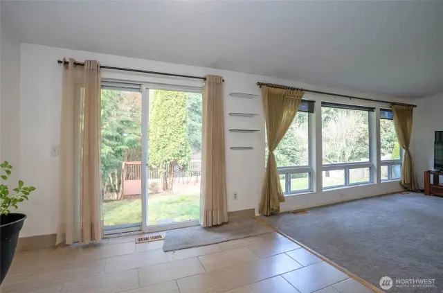 View of the living area from the dining space, featuring a sliding door that opens to the backyard and spacious deck overlooking the Olympic View Park trail system.