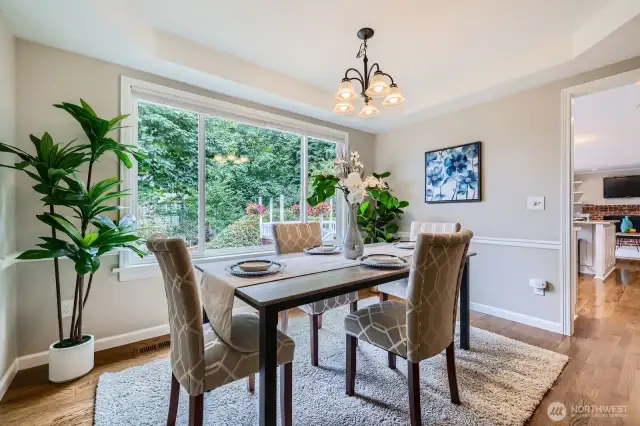 Formal dining room with tray ceiling and expansive window overlooking the backyard. Warm wood floors and updated light fixture.