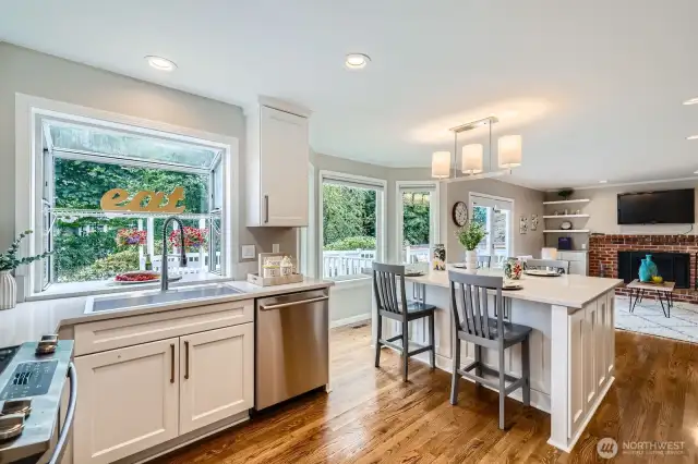 Updated kitchen with white cabinetry, quartz countertops, and stainless steel appliances. Garden window and bar seating at center island.