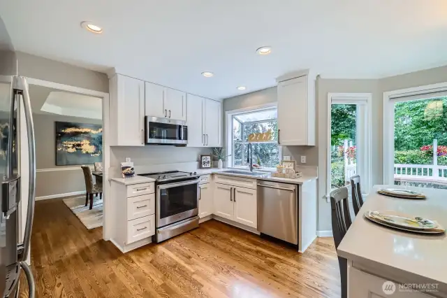 Efficient kitchen layout with ample cabinet storage, modern appliances, and direct access to dining area. Multiple windows bring in greenery and light.