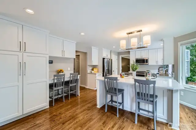 Kitchen includes a built-in desk area with overhead storage and workspace. Seamless transition to adjacent hall and garage access.