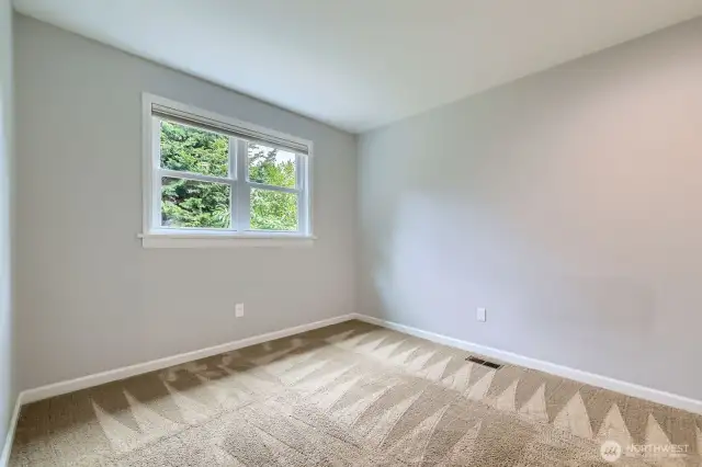 This upstairs bedroom features fresh paint, soft carpeting, and a large window overlooking the private backyard greenery.