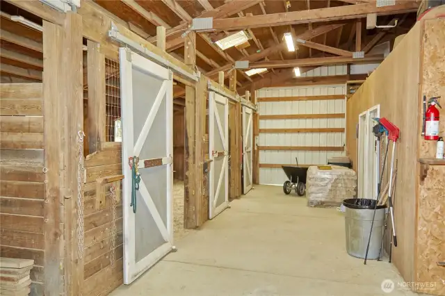 The barn features four spacious stalls, a dedicated tack room, and a utility room for added convenience.  Off to the right is a lifted hay storage area.
