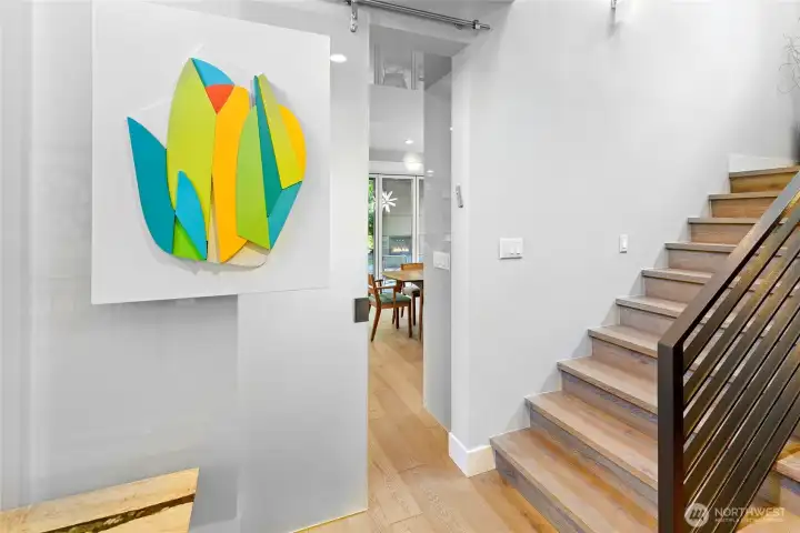 Coates Design artisan glass barn door dividing the foyer from kitchen and living areas (glass barn door holds hanging art, this piece does not convey).