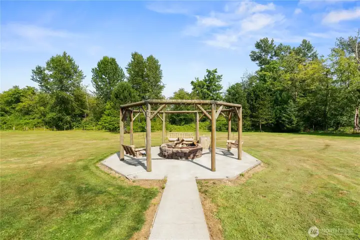 Outdoor gathering area features a covered timber pergola, built-in fire pit, and swing seating Outdoor gathering area features a covered timber pergola, built-in fire pit, and swing seating