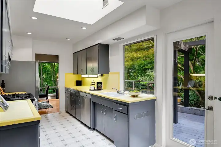 Kitchen with skylight, bright yellow tile counters, stainless steel appliances.  Service door to deck and access to garage.