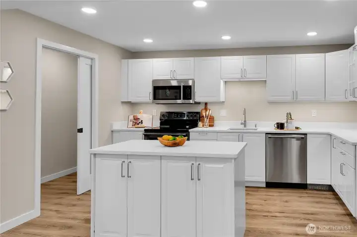 Brand new IKEA kitchen designed for form and function featuring a central island, sleek cabinetry, stainless appliances.  A pocket door reveals a dedicated laundry nook with space for stackable washer and dryer.