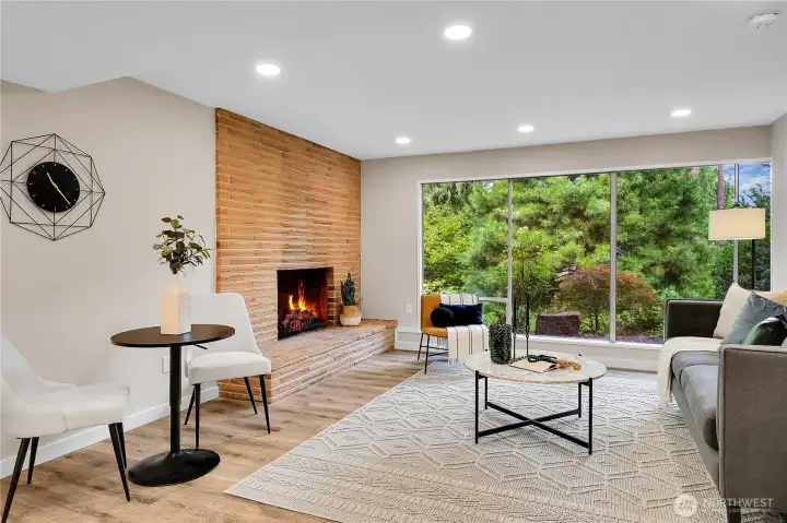 Open concept great room.  Brick fireplace anchors the space while nearly floor to ceiling windows stretch across the length of the apartment, bringing in natauaral llight and framing views of the lush surroundings.