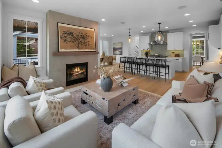 Expansive great room featuring wide-plank hardwood floors, designer lighting, and a sleek gas fireplace. Open concept design seamlessly connects the living, dining, and chef’s kitchen areas.