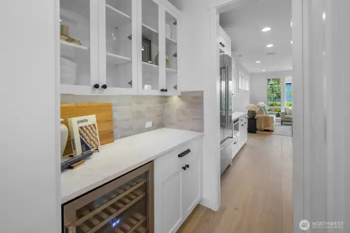 Butler’s pantry with marble counters, custom cabinetry, designer tile backsplash, and beverage refrigerator. Perfect for prep, storage, and entertaining ease.