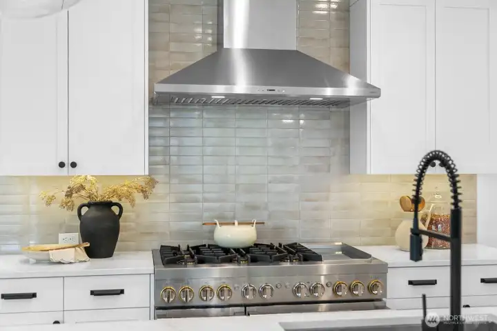 Professional-grade gas range with stainless steel hood, quartz counters, and artisan tile backsplash. A chef’s dream setup for culinary creativity.