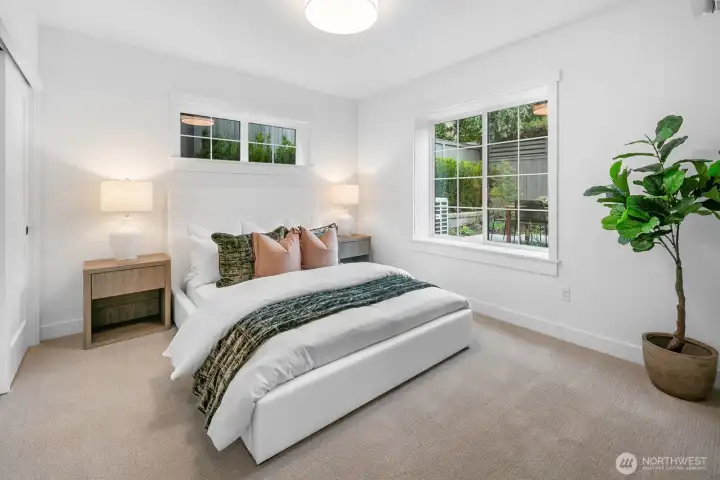 Private lower-level bedroom with oversized windows, ample closet space, and serene views of the landscaped yard.