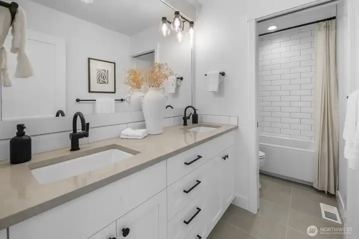 Stylish full bath with dual vanity, quartz counters, subway tile tub surround, and modern matte black fixtures.