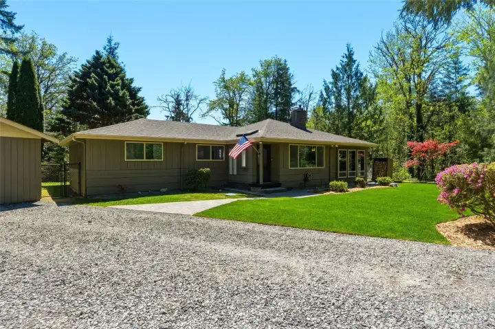 Wide-angle view of the home’s front exterior highlighting mature landscaping, open yard space, and peaceful wooded surroundings.