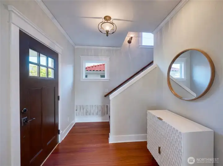 Welcoming foyer with rich Brazilian hardwood floors, crown molding, classic craftsman-style front door, and elegant staircase — a first impression that sets the tone for the quality found throughout.