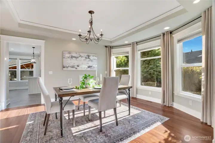 Elegantly appointed dining room with tray ceiling, designer chandelier, and bay windows framing a breathtaking sunset — the perfect setting for memorable gatherings.